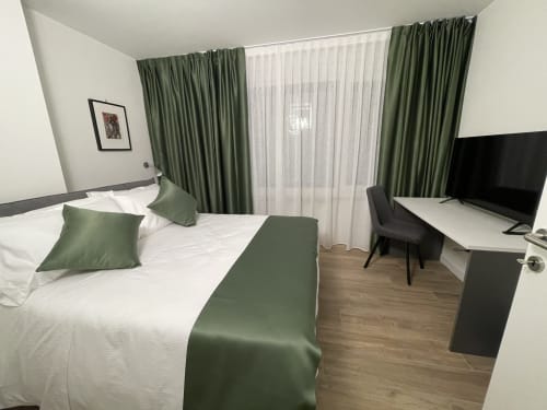 Camera moderna al Saint Michel Gorizia con letto matrimoniale, accenti verdi, scrivania, TV e accesso a balcone con vista sulla città