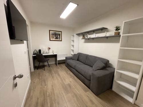 Camera moderna dell'hotel Saint Michel Gorizia con divano grigio, scrivania, mensole e TV a schermo piatto