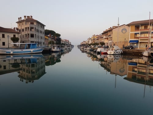 Tranquillo waterfront del canale a Gorizia con edifici storici, barche e riflessi specchiati a San Michele