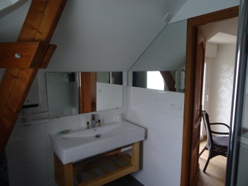 Salle de bain mansardée moderne avec lavabo blanc, grand miroir et poutres en bois apparent au CafecouetBreizh B&B à Guipry-Messac