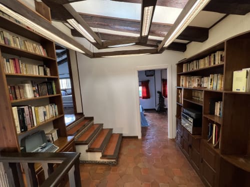 Salón biblioteca con vigas de madera, estanterías, escritorio y suelo de terracota en villa de lujo cerca de Puy du Fou