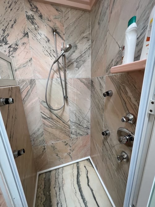 Elegante cabina de ducha revestida de mármol con lluvia cenital, múltiples chorros corporales y repisa de amenidades en Villa Luxury PLUS