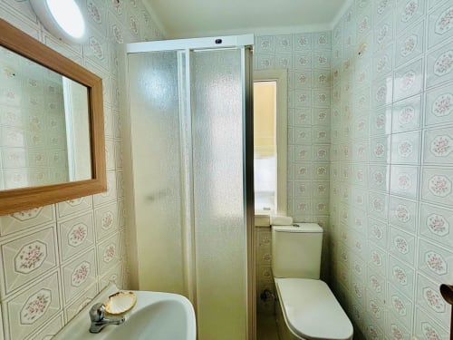 Baño moderno en el apartamento Breixo, Baiona con ducha, lavabo, inodoro, espejo y paredes con azulejos florales
