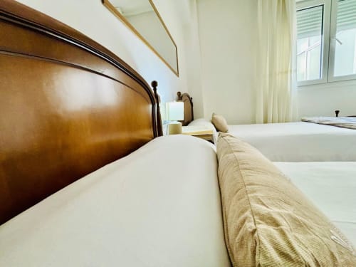 Dos camas individuales con ropa blanca y cabecero de madera en el apartamento Breixo, frente al mar de Baiona