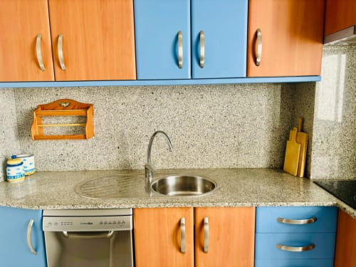 Cocina moderna en apartamento de Baiona con muebles azules y naranjas, encimera de granito y fregadero de acero inoxidable