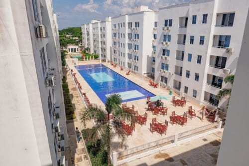 Vista aérea de la piscina y patio de Olamar Living con edificios blancos, piscina azul, palmeras y detalles en rojo