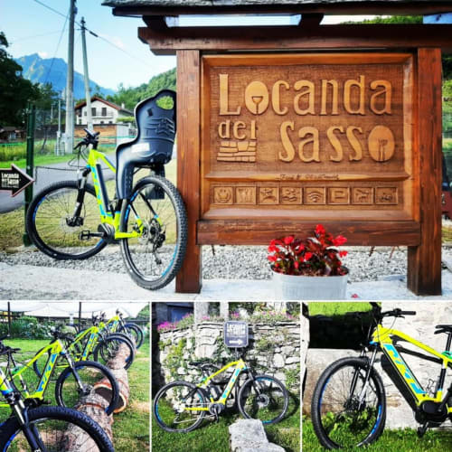 E-bike gialle presso la Locanda del Sasso a Crodo, Italia con insegna in legno e sfondo montano