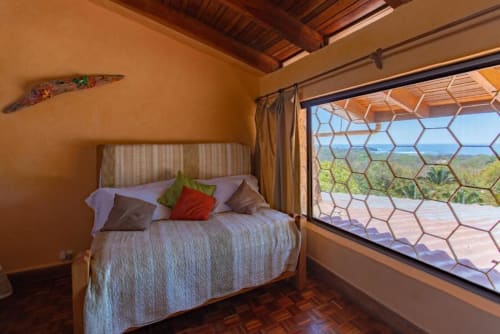 Rana room at Villa Mango B&B in Nosara with ocean view from bed, warm terracotta walls, and hexagonal window screens
