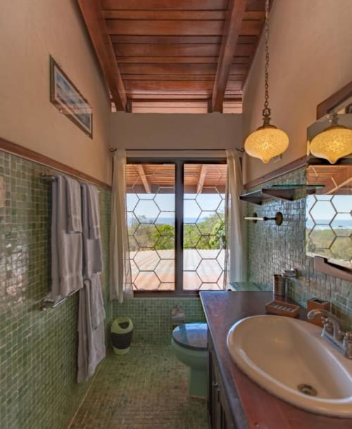 Modern bathroom at Villa Mango B&B in Nosara with green tile, round sink, ocean view through hexagonal patterned doors