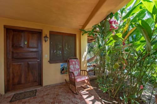 Tucan room porch at Villa Mango B&B in Nosara with wooden door, pink chair, and lush garden plants