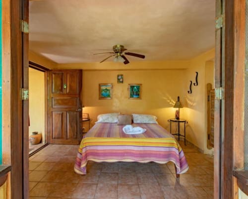 Bright yellow bedroom at Villa Mango B&B in Nosara with colorful bedding, ceiling fan, and wooden furnishings
