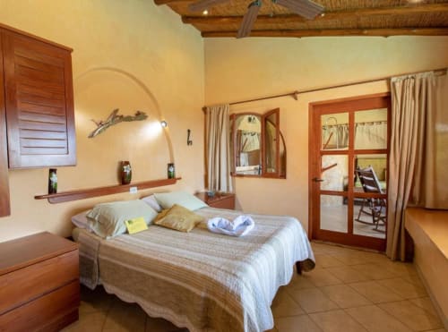 Congo room at Villa Mango B&B in Nosara with garden view, featuring wooden bed frame, cream walls, and rustic Costa Rican