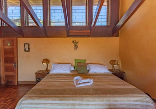 Rana room at Villa Mango B&B in Nosara with wooden bed, orange walls, skylights, and sea view windows