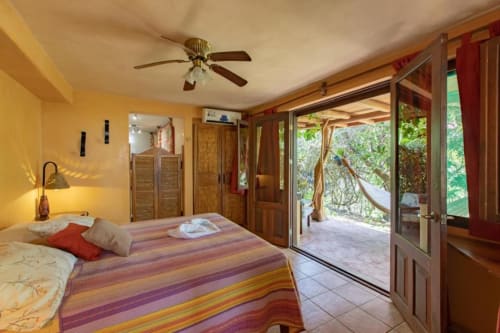 Bright yellow bedroom at Villa Mango B&B in Nosara with striped bedding, ceiling fan, and garden view doors