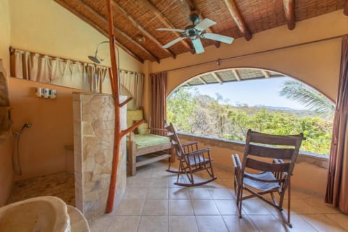 Villa Mango B&B bedroom in Nosara, CR with jungle view, open bathroom, ceiling fan, and rocking chairs