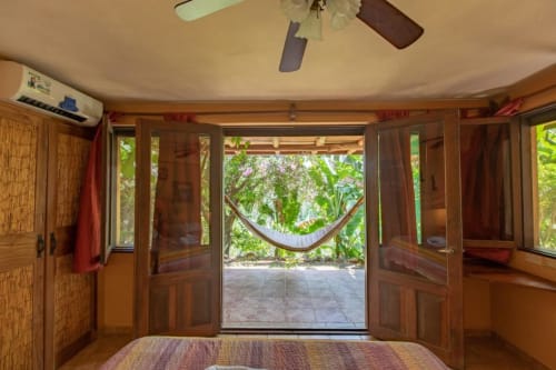Villa Mango B&B bedroom in Nosara with wooden furnishings, ceiling fan, and garden view through glass doors