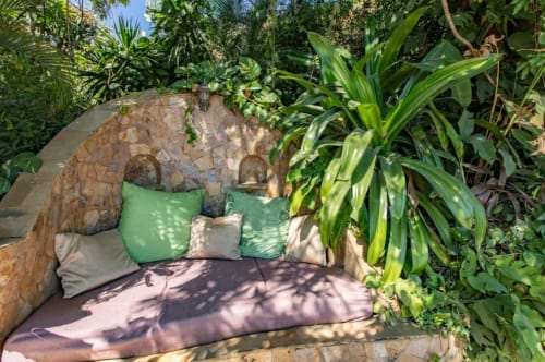 Cozy outdoor garden seating nook at Villa Mango B&B in Nosara with stone structure, green cushions, and tropical plants