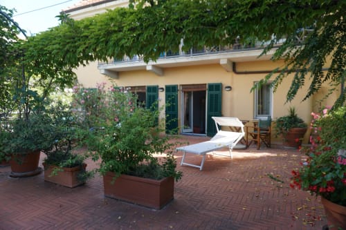 Sonnige Terrasse des Hotel Beau Rivage Alassio mit Liegestühlen, Topfblumen und gelbem Gebäude mit grünen Fensterläden
