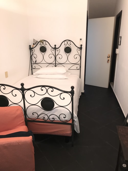 Kompaktes Einzelzimmer im Hotel Beau Rivage Alassio mit verziertem Schmiedeeisenbett, weißer Bettwäsche, korallenfarbener Decke und schwarzen Fliesen