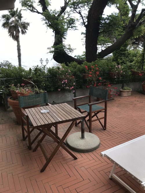 Gartenterrasse des Hotel Beau Rivage in Alassio mit Holzmöbeln, blühenden Pflanzen und ausgewachsenen Bäumen