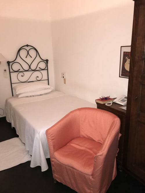 Modernes Zimmer im Hotel Beau Rivage in Alassio mit schmiedeeisernem Bett, weißer Bettwäsche und korallfarbener Sessel