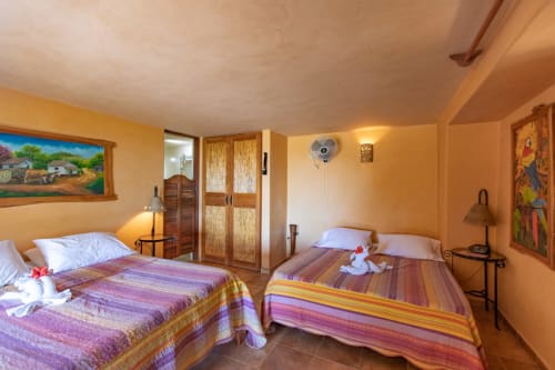 Lora room at Villa Mango B&B in Nosara with two beds, colorful striped bedding, and warm yellow walls