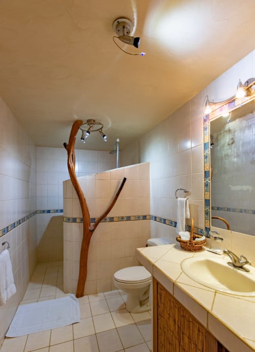 Bathroom at Villa Mango B&B Nosara with white tile, wooden shower fixture, vanity sink, and decorative basket