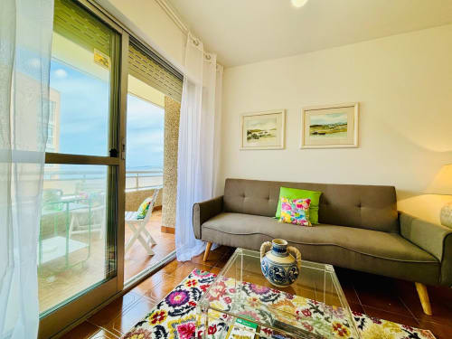 Moderno salón con sofá marrón, mesa de cristal y obras de arte. Terraza con vistas al mar y las Islas Cíes, Baiona.