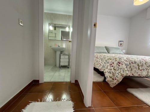 Dormitorio del apartamento Baiona con baño en suite, ropa de cama floral y suelo de baldosas de barro