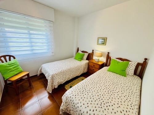 Habitación doble con almohadas verde brillante, muebles de madera y vistas al mar en apartamento de Baiona