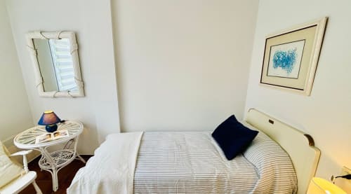 Acogedora habitación en apartamento Holibai, Baiona con cama rayada, almohada azul marino, muebles blancos y obra de arte con vista al mar