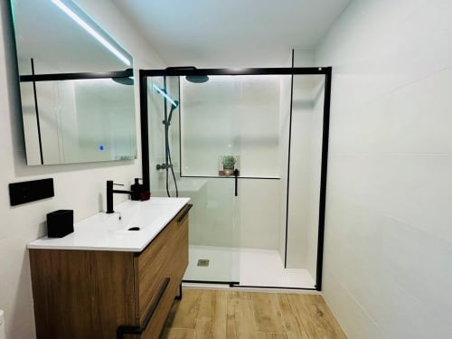 Baño moderno del apartamento Holibai con ducha abierta, tocador de madera y paredes con azulejos blancos en Baiona