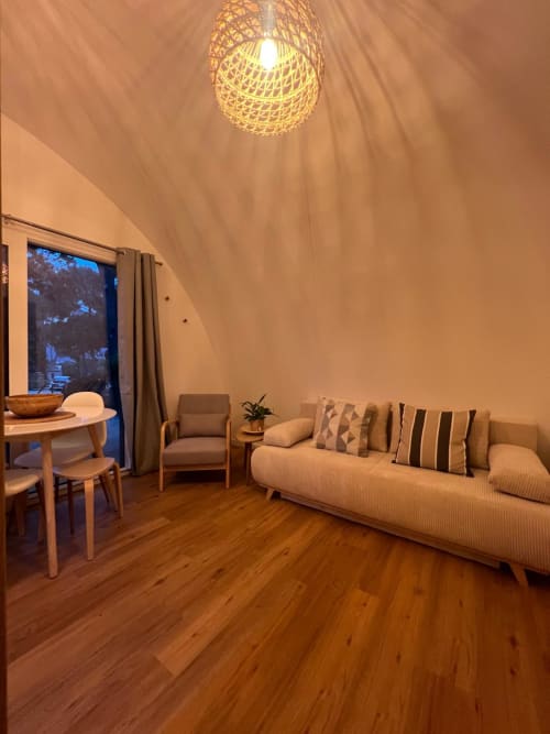 Appartement moderne au Camping La Lézardière avec canapé, coin repas, lampe suspendue tressée et vue sur le jardin
