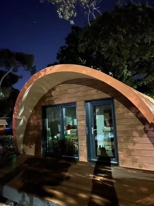 Pod d'hébergement aux formes courbes du Camping La Lézardière, façade bois, portes vitrées et vue sur le jardin la nuit
