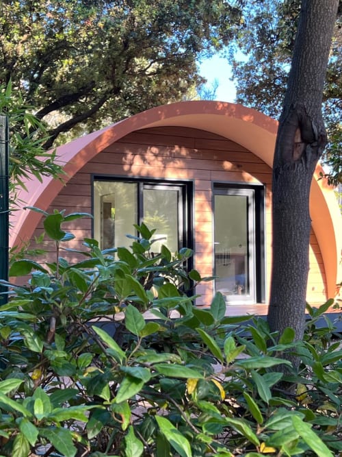 Façade moderne en terre cuite du camping La Lézardière avec toit en arche, portes vitrées et végétation de jardin