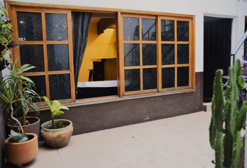 Entrada del apartamento hotel LLUNA con ventanas de marco de madera, interior amarillo, plantas en maceta y cactus en Oaxaca de Juárez