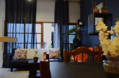 Sala de estar del apartamento LLUNA en Oaxaca con paredes azules, cortinas oscuras, cojines coloridos, muebles de madera y flores amarillas