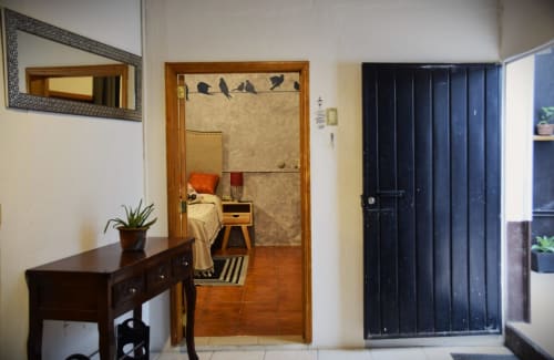 Entrada del apartamento LLUNA en Oaxaca con vista al dormitorio, puerta de madera oscura, espejo, planta y acceso al jardín