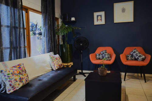 Sala moderna del apartamento LLUNA en Oaxaca con paredes azul marino, sillas naranjas, sofá negro y vista al jardín