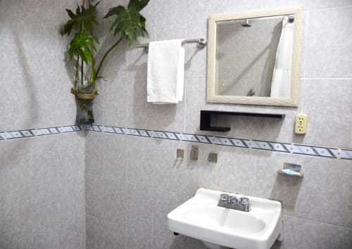Baño moderno del hotel LLUNA en Oaxaca con lavamanos blanco, paredes de azulejos, espejo enmarcado, toallero y plantas decorativas