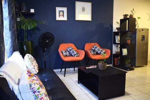 Moderno salón LLUNA en Oaxaca con sillas naranjas, paredes azules, mesa negra y plantas en macetas