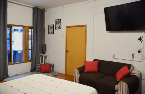 Apartamento LLUNA en Oaxaca con sofá oscuro, cojines rojos, cama, puerta amarilla, TV y vista al jardín