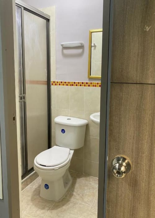 Baño moderno en hotel Casa Mango de Cali con inodoro blanco, ducha y cenefa de azulejos decorativos