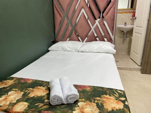 Habitación del hotel Casa Mango en Cali con cama, cabecera rosa, almohadas blancas y toallas enrolladas sobre camino floral