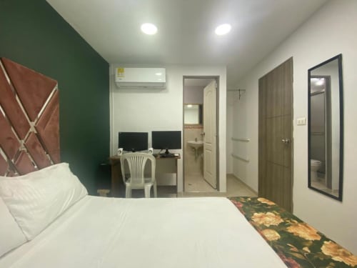 Habitación del hotel Casa Mango en Cali con cama, escritorio de trabajo con monitores, pared de acento verde y entrada al baño