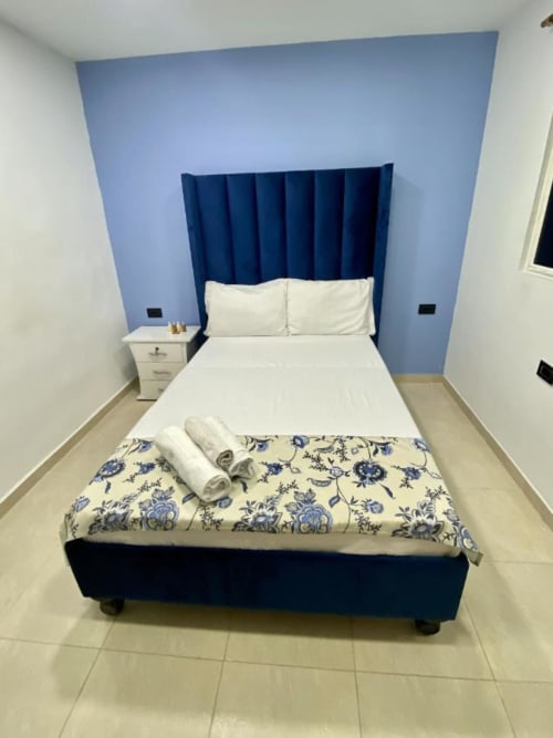Dormitorio moderno en hotel Casa Mango de Cali con pared de acento azul, cama tapizada en azul marino y ropa de cama blanca