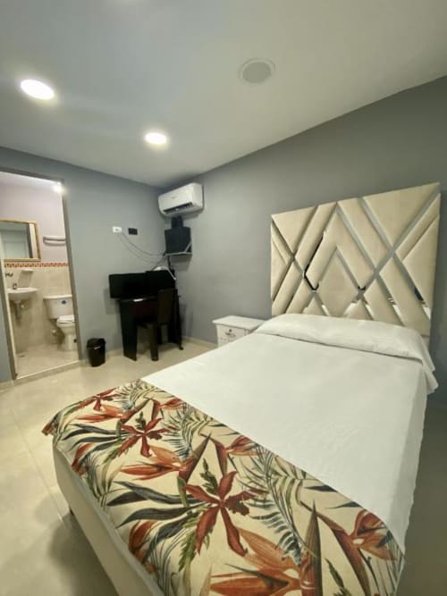 Habitación moderna en el hotel Casa Mango en Cali con cama blanca, manta con estampado, cabecero geométrico y baño ensuite