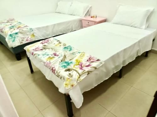 Dos camas gemelas con sábanas blancas y colchas florales en el hotel Casa Mango de Cali