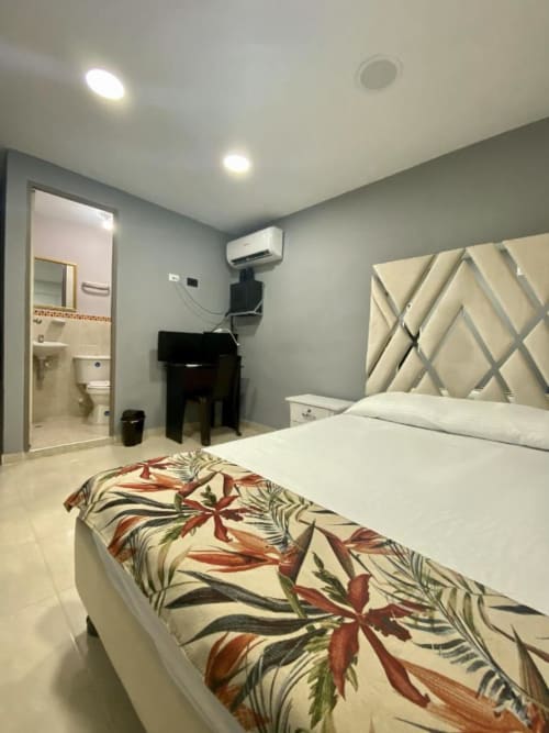 Habitación moderna en hotel Casa Mango de Cali con cama blanca, cabecera geométrica, baño privado y aire acondicionado