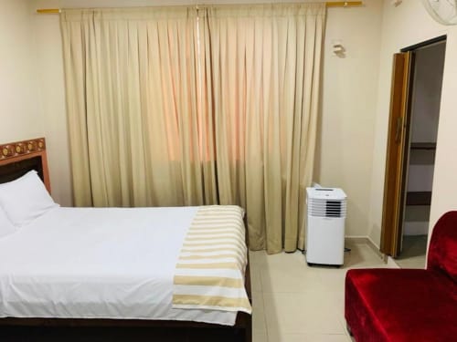 Habitación del hotel Casa Mango en Cali con cama, ropa de cama blanca, manta a rayas, aire acondicionado portátil, cortinas color crema y silla roja